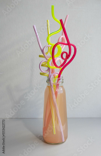A glass bottle of pink drink with colorful straws. Cocktail straw day.