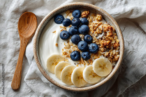 healthy breakfast bowl with creamy yogurt granola clusters fresh blueberries and banana slices served in rustic ceramic dish on soft fabric background perfect for wellness and food content