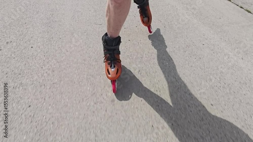 Close-up view of male legs in orange inline blades boots moving on the road. 