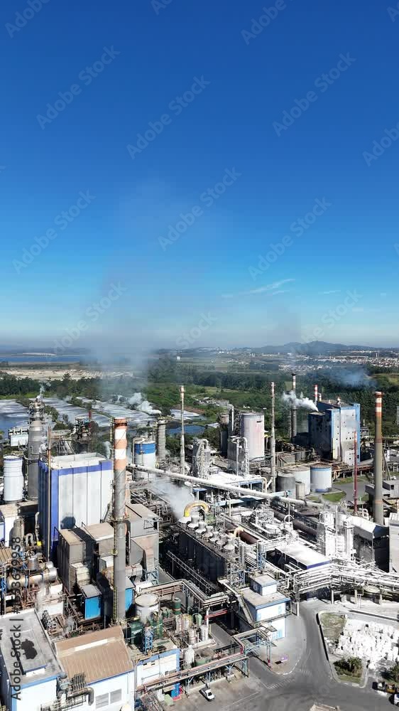 Imagem aérea vertical mostra indústria de papel e celulose com destaque para chaminé em operação, ilustrando impactos ambientais e emissões poluentes do setor fabril