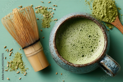 top view of a ceramic cup filled with frothy matcha latte next to bamboo whisk and green matcha powder on pastel background showcasing traditional tea preparation and natural ingredients
