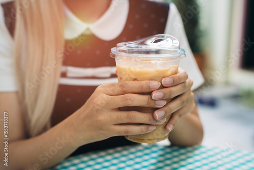 Hand holding coffee. Hands Holding Iced Coffee Drink in a Clear Plastic Cup on a Colorful Table Under Natural Light