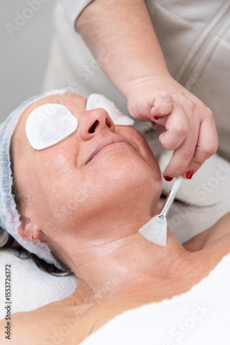Beautician applying cream on woman's neck with brush during skincare treatment
