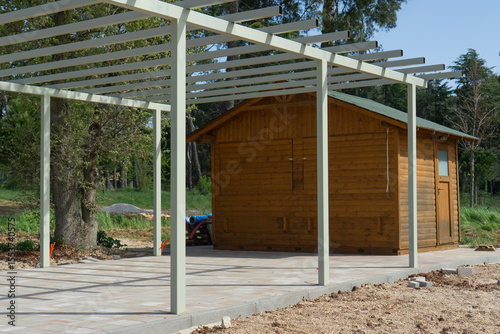 Metal pergola in front of a wooden cabin or shed in an outdoor setting, concept of outdoor living, recreational architecture, garden design.