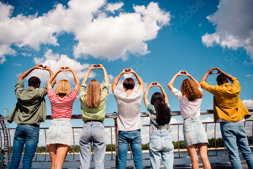 Group of young friends outdoors showing heart gestures on a sunny day, celebrating friendship and unity together