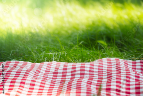Red picnic checkered towel plaid on grass, empty space food advertisement summer design background, template.