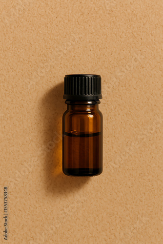 Small amber glass vial with black cap on a textured light brown background, ideal for showcasing essential oils or natural serums