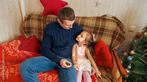 Happy father and daughter hugging and sitting on the sofa near the Christmas tree at home