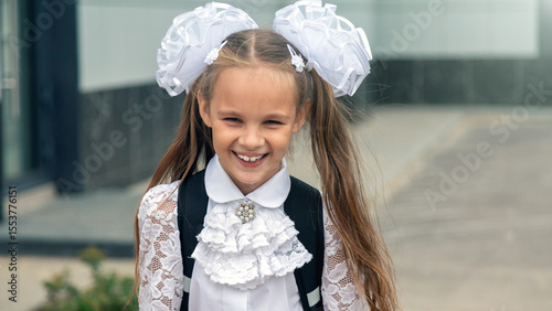 Cheerful girl wear uniform posing with backpack near school building outdoor, smiling to camera.