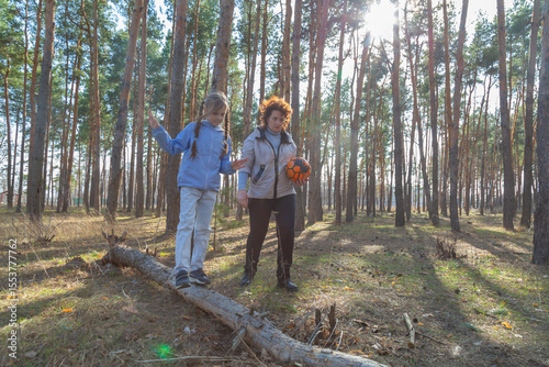 Grandmother and granddaughter walking with a ball in the forest in sunny day.