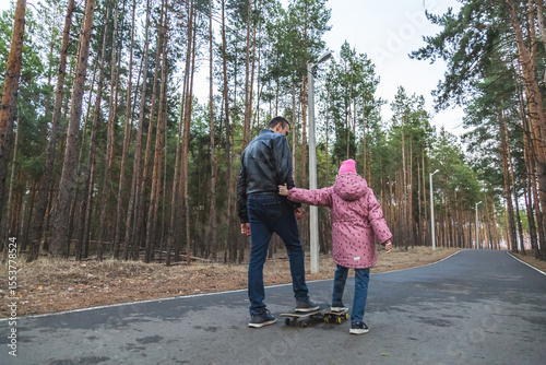 Father and daughter riding skateboards in the forest.