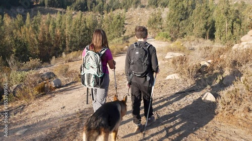 Latin American teen hikers are walking with their german shepherd dog on a mountain trail