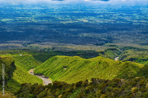 View from the alpine region of the heavily eroded northeastern slopes of the volcano Taranaki on North Island, New Zealand. In the far distance flat land with meadows and agricultural fields
