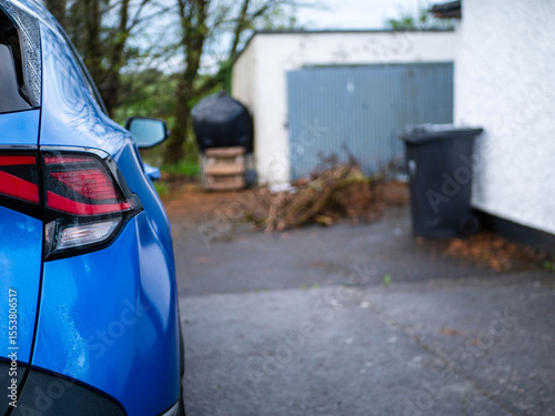 Blue car is back in a back yard of and old house with garage and outdoor oil heating tank and waste bin. Selective focus. Rural country area background. Living out of town concept.