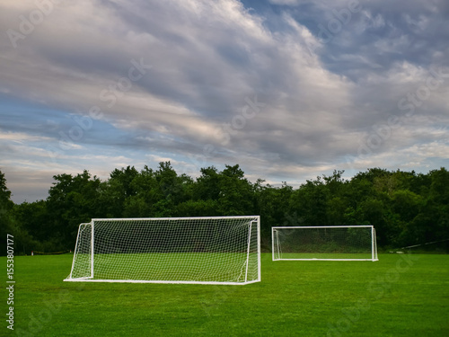 Clean cut football or soccer training ground with two goal posts, dark trees and dramatic sky in the background. Popular world sport. Team development area. Nobody.