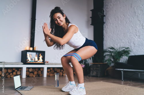 Woman touches laptop screen excitedly while holding water bottle after completing resistance-band workout, capturing tech‑enabled fitness achievement and digital tracking.