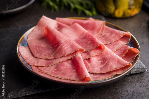 Sliced beef pastrami on plate on black table.