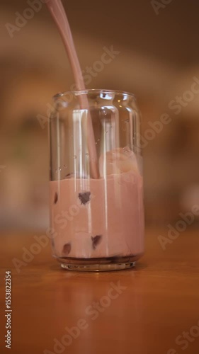 Pours a milkshake into a glass of ice