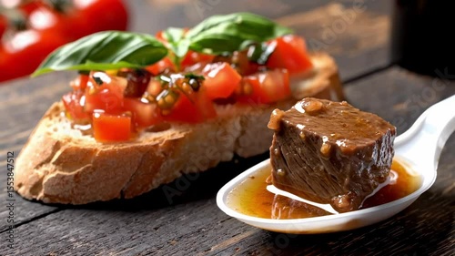 Bruschetta with tomato basil topping and a cube of braised meat on a spoon Set on a wooden table