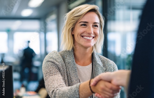 Friendly businesswoman with blonde hair smiling and shaking hands du professional meeting in modern corporate office environment photo