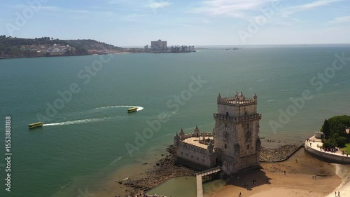 Aerial drone shot of Belem Tower with boats moving nearby on the Tagus River in Lisbon, highlighting the iconic monument and water activity in the area