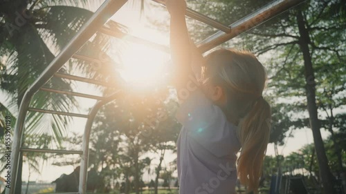 child are moving away from camera on horizontal ladder on sports ground, sun is shining into camera. A bottom-up view of children doing sports exercises than jump off.