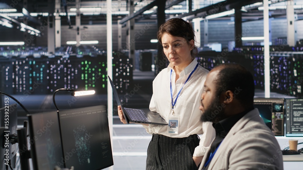 Fototapeta premium Happy data center manager providing positive feedback to engineer developing neural networks software on computer. Cheerful supervisor pleased by employee work implementing AI in server room, camera A