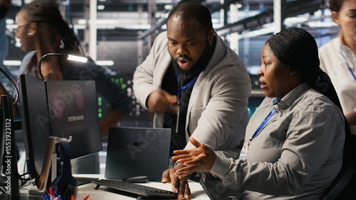 Scared data center technicians reacting to virus warning on PC display, scrambling to launch emergency response protocol. Admins run around server room, urgently trying to fix hacked systems, camera A