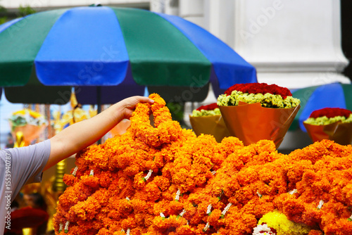 A tourist’s hand placing marigold garlands as an offering for blessings at the Erawan Shrine in Ratchaprasong, Bangkok, Thailand.