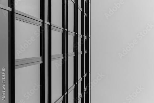 Black and white photo of a modern glass building facade with strong geometric lines. The image emphasizes architectural structure and urban design.
