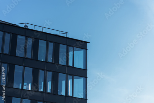 Contemporary office building with large glass windows under clear blue sky, suitable for business or architecture themes. The image highlights modern urban design and corporate environment.