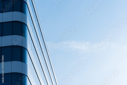 Photo shows a contemporary office building with curved glass windows and white panels. The structure is set against a clear blue sky, emphasizing modern architecture and urban business environments.