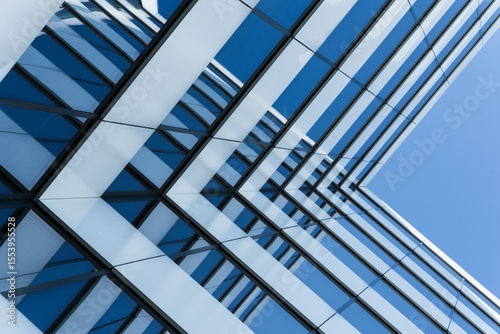 Close-up view of a contemporary glass office building with geometric lines reflecting a clear blue sky. The image emphasizes modern architecture and urban design for business or construction concepts.
