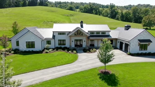 Aerial view of a modern farmhouse with white exterior and a long driveway in a field