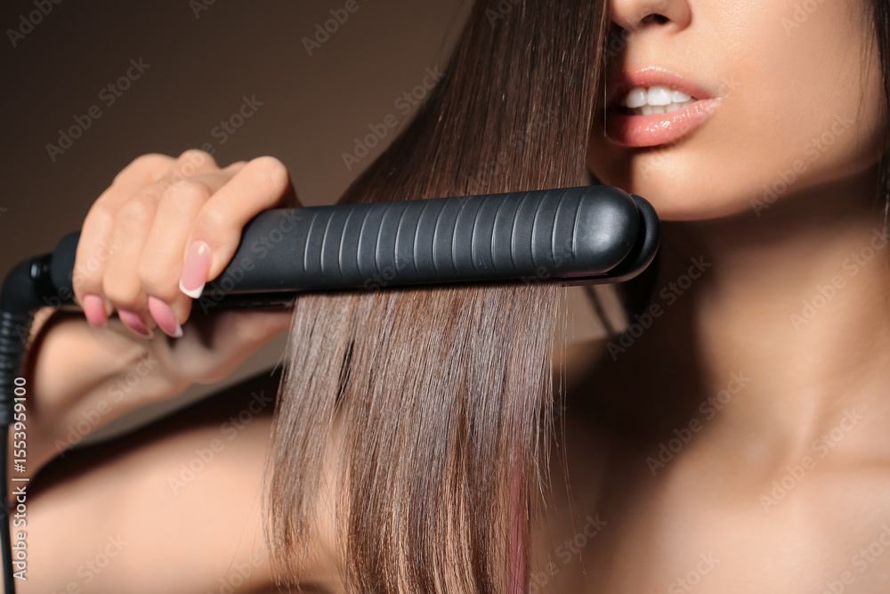 Obraz premium Beautiful young woman straightening hair on beige background, closeup