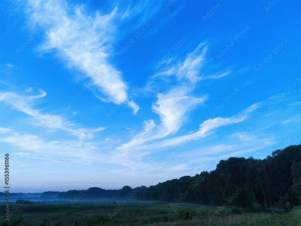 Fototapeta premium Blue Sky with Unique Cloud Formations Over Green Landscape