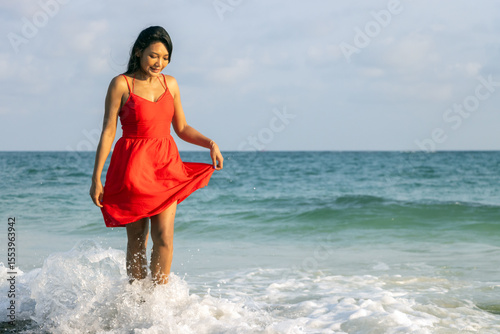 A woman in a red dress walk in waves at sea shore