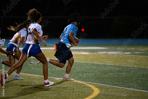 Εκτύπωση καμβά Girls flag football player runs toward end zone with ball as opponents chase in pursuit, intense youth sports game, school competition, team strategy, speed and agility under stadium lights