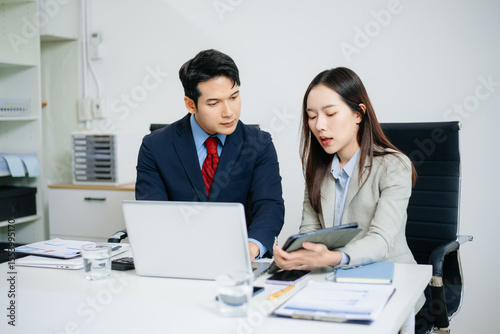 Young Asian businessman and colleague using laptop and tablet while discussing project in modern office. Consulting, teamwork, strategy