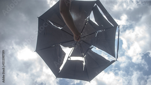 A girl in a black umbrella against the blue sky with white clouds
