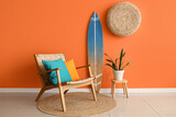 Armchair, houseplant and surfboard near orange wall in interior of living room