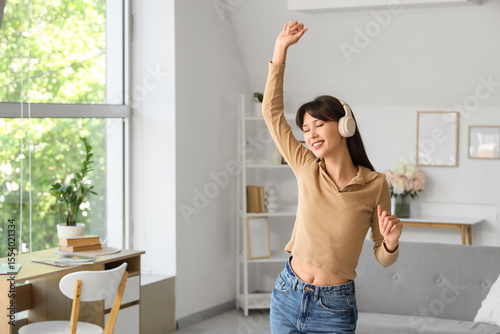 Smiling young woman in headphones dancing at home