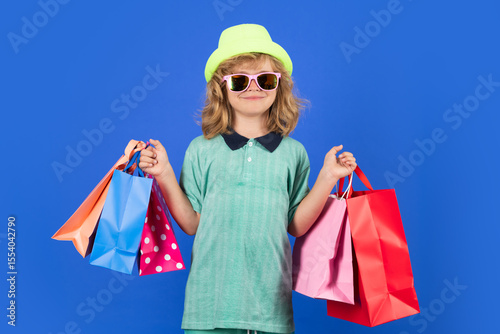 Kid boy in fashion clothes goes shopping. Kid with shopping packages. Shopper child with carrying shopping bags.