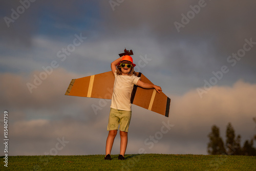 Kid pilot aviator with with paper wings dreams of traveling in summer in park outdoor.
