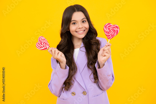 Cool teen child with lollipop over yellow isolated background. Sweet childhood life. Teen girl with yummy lollipop candy. Happy teenager, positive and smiling emotions of teen girl.