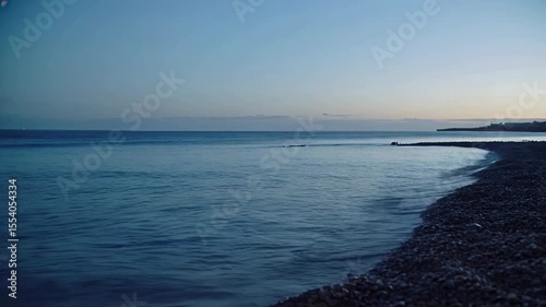 Tranquil seaside view featuring gentle waves lapping at pebbled shore during twilight hours