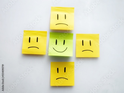 A green sticky note with a smiling face placed between two yellow sticky notes with angry faces, highlighting the contrast between positivity and negativity