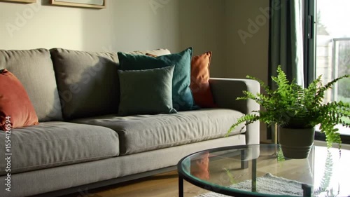 Modern Living Room Interior with Sofa, Colorful Pillows, Glass Table, and Plant Bathed in Natural Light