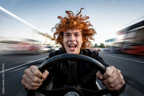 A red-haired guy holds the steering wheel of a car in front of him and rushes along the highway.