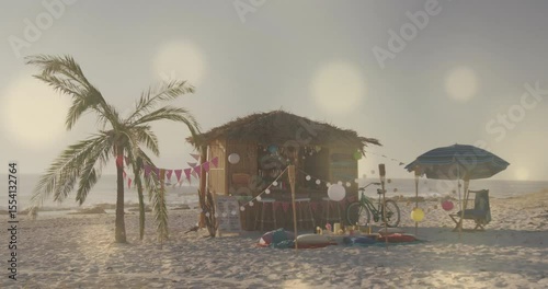 Rising sun sending golden rays warming thatched-roof beach hut scene and shifting reflections